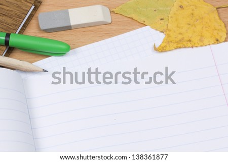 Opened school notebook and pencil, pen, eraser, leaves