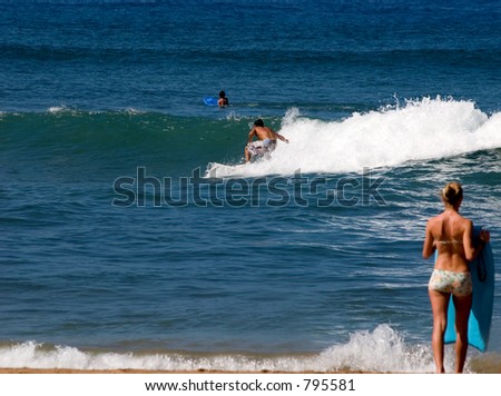 Learning to surf in Maui with girl on Beach watching. Focus is on the surfer