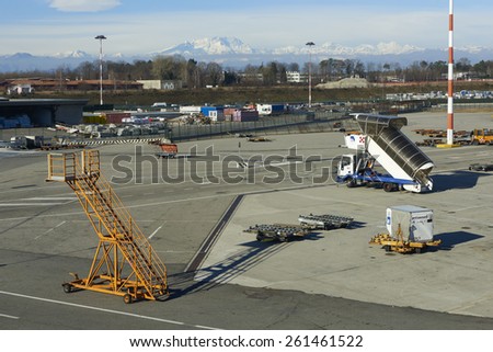 Ferno, Italy - January 01, 2015: passengers boarding ramps and other ground support equipment on the apron at Malpensa Airport. In the background the Monte Rosa Massif.