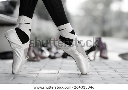 Closeup of a ballerina\'s feet in Pointe on the street, different kind of shoes in background