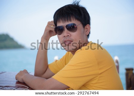 Portrait of a young man in yellow T-shirt wears sunglasses on the boat floating on the sea