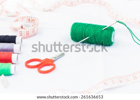 Green spool of thread with needle and colored thread, scissors and centimeter
