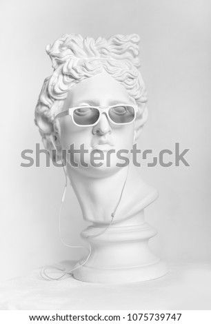 Gypsum statue of Apollo\'s head. Man. Statue. Plaster statue of Apollo\'s head in earphones and white sunglasses.