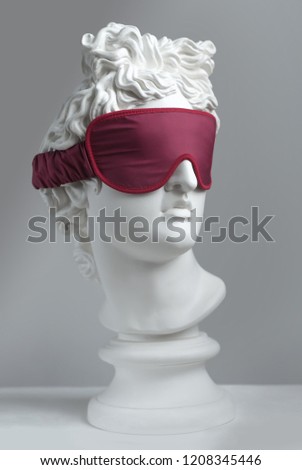 Statue. Isolated. Red sleeping mask.  Gypsum statue of Apollo\'s head. Man. Statue. Plaster statue of Apollo\'s in red sleep mask.