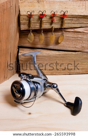 Fishing reel with metal lures on the wooden table.