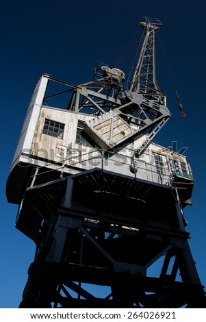 Vintage Crane on Dockside in Historical Bristol, England. The photo is taken from below with a wide angle to exaggerate the form of the crane against the crystal clear blue sky.