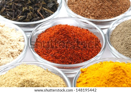 Variety of raw Authentic Indian Spices Powder on glass bowl isolated on white background in full-frame. Focus on chilli powder.