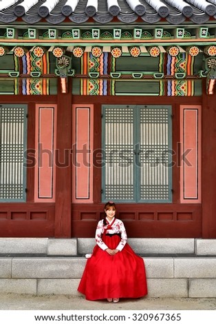 SEOUL, KOREA - SEPTEMBER 19, 2015: Young Korean woman in traditional dress sitting on traditional building\'s stairs.