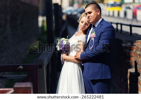 the bride and groom with a bouquet standing in the sun and closed eyes