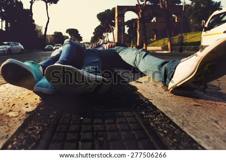 close up shoes of two people lying on the curb between two roads in Rome