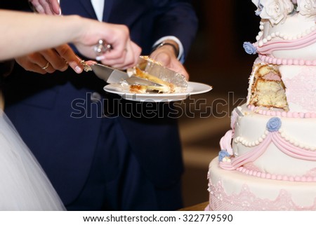 Happy elegant bride in white dress and stylish groom cutting wedding cake close-up
