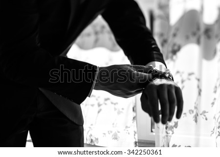 Handsome confident groom putting on watch in suit closeup black and white