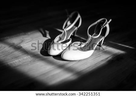 Elegant stylish white leather bride shoes on wooden floor closeup black and white