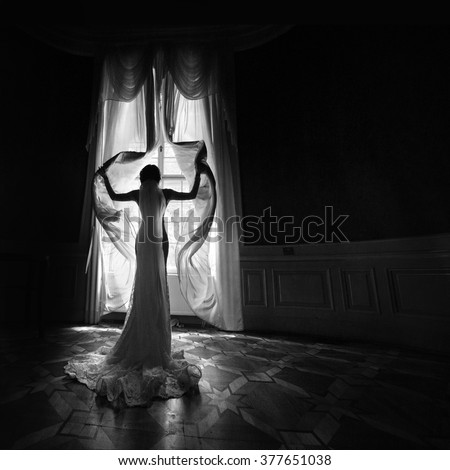 Gorgeous happy bride in white dress opening curtains in theatre b&w