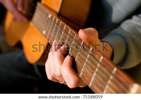 Brown guitar in hands of the guy playing it. Shallow depth of filed