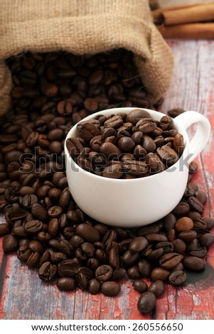 Coffee beans drop out of the bag in a cup on a red wooden table