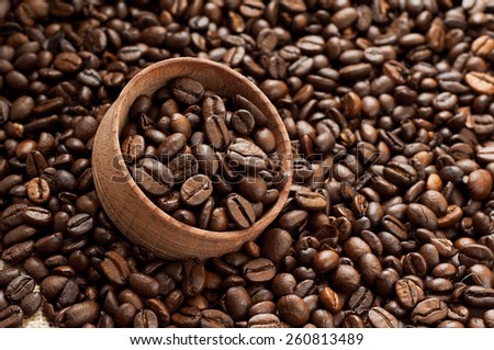 Coffee beans in a wooden bowl for storage on scattered coffee beans