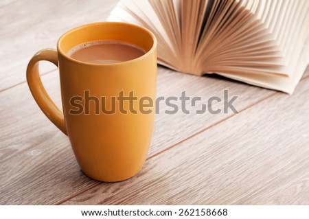 Coffee with milk in a large cup standing on wooden table next is an open book