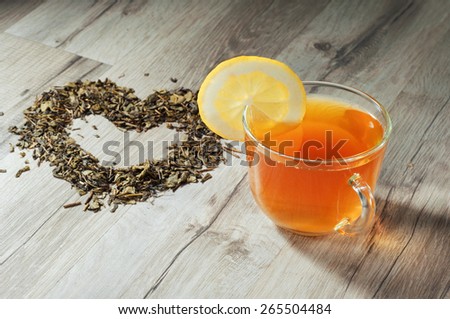 Cup of tea on a wooden table. Next to a cup of tea, heart made of dried tea leaves