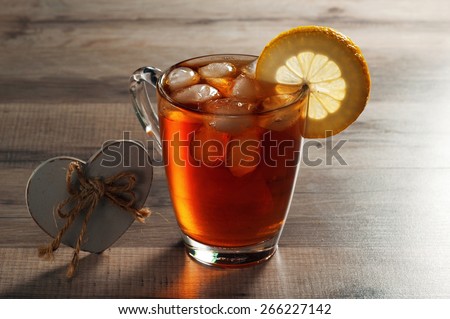 Black tea with ice and a slice of lemon in a glass mug. Next to a cup of tea wooden heart