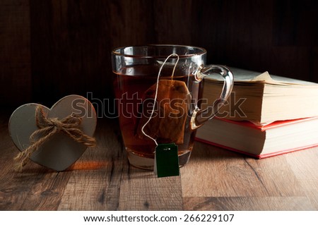 Tea, black, classic, a glass mug. With mugs hanging tea bag.Next to the tea two books and a wooden heart