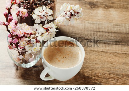 Fragrant coffee on a wooden table. next to a cup of coffee, a jar of coffee beans and a bouquet of blossoming apricot