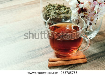 Black tea in a cup on a wooden table. next to a cup of tea, worth a bouquet of flowers of blossoming apricot and are two cinnamon sticks