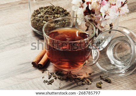 Black tea in a cup on a wooden table. next to a cup of tea, worth a bouquet of flowers of blossoming apricot, two cinnamon sticks and scattered dry tea leaves