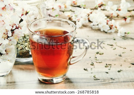 Black tea in a cup on a wooden table. Next to a cup of tea bouquet of blossoming apricot and scattered dry tea leaves