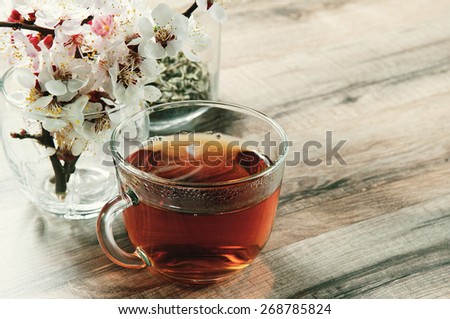 Black tea in a cup on a wooden table. Next to a cup of tea bouquet of blossoming apricot