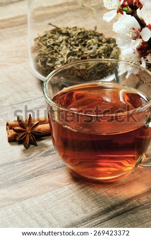 Black tea in a cup on a wooden table. next to a cup of tea, worth a bouquet of flowers of blossoming apricot and are two cinnamon sticks