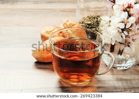 Black tea in a cup on a wooden table. next to a cup of tea, worth a bouquet of flowers blooming apricot and three fresh croissants