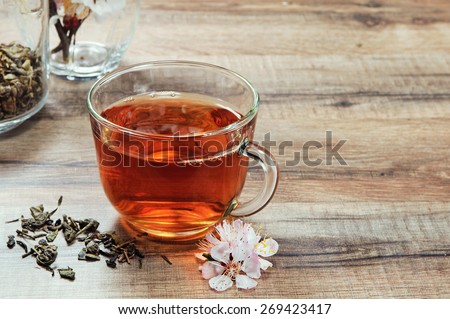 Black tea in a cup on a wooden table. Next to a cup of tea bouquet of blossoming apricot and scattered dry tea leaves