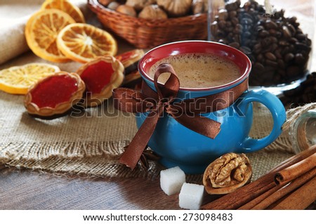 A cup of coffee costs on a wooden table. About a cup of coffee is cinnamon, walnut, dried orange slices and two pieces sugar. The festive atmosphere