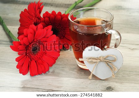 black tea with beautiful flowers gerbera. Next to a cup of tea is a small, wooden heart