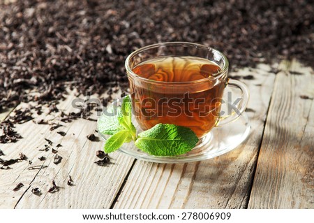Black tea in a glass cup and saucer on a wooden table. Next to a cup of black tea scattered dry tea