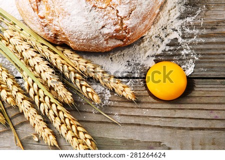 Wooden table sprinkled with flour. On the table lay spikelets of wheat, freshly baked bread and an egg yolk. Ingredients for making fresh bread. top view