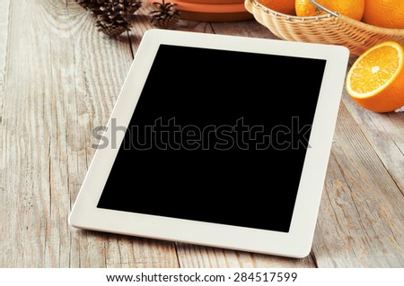 White tablet computer  with a black screen and oranges on the wooden table