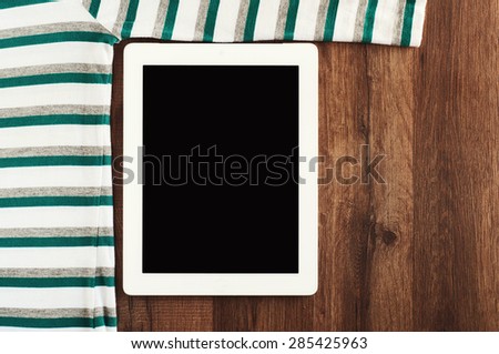 White tablet computer with a striped sweater on a wooden table. top view