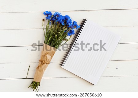 beautiful bouquet of blue wildflowers with an empty memo pad for notes on a white wooden table