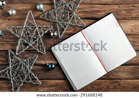 Blank open notebook for records on the old wooden table. Near the notepad lies  New Year Three stars and toys
