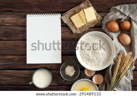 On the old wooden table Open notebook for notes and ingredients for baking - flour, milk, eggs, butter. View from above. Rural background with free text space. Ingredients for the dough