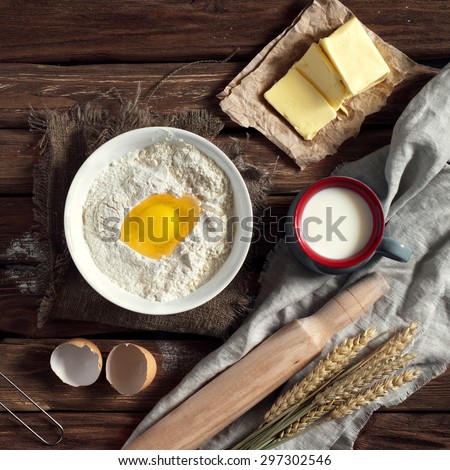 Baking ingredients - flour, egg, butter, milk on vintage wood table. Top view. Rustic background with free text space.  Ingredients for the dough