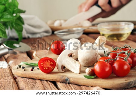 Food ingredients for pizza or spaghetti. Fresh cherry tomatoes, mushrooms, garlic, basil leaves, flour, olive oil. Against the background of man hand cut mushrooms. Close up. Copy space