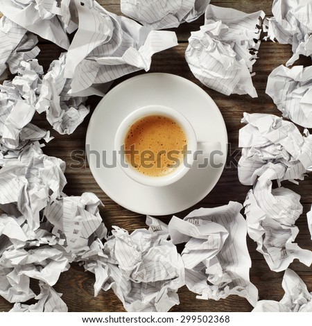 A cup of black coffee on the wooden table. Around the cup of black coffee lies lot crumpled paper. top view