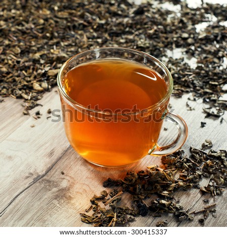 glass cup with tea is on wooden table. Next to a cup of tea scattered tea leaves.