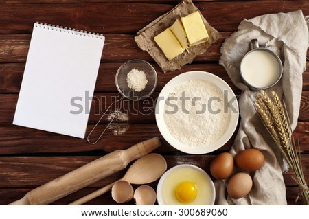 On the old wooden table Open notebook for notes and ingredients for baking - flour, milk, eggs, butter. View from above. Rustic background with free text space. Ingredients for the dough