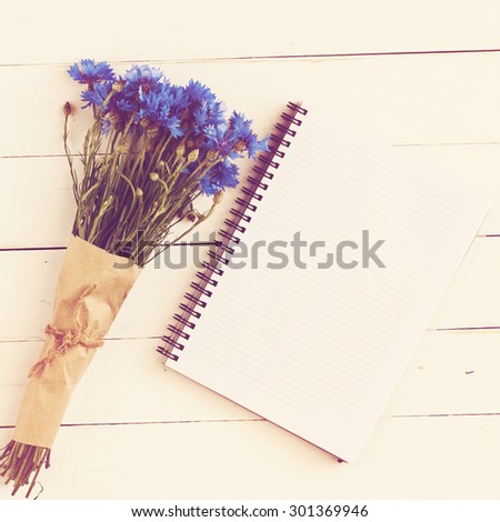 beautiful bouquet of blue wildflowers with an empty memo pad for notes on a white wooden table