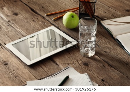 tablet computer with a blank screen on the wooden table with a glass of ice water, notepads, pencils and apple. Top view. Copy space. Free space for text.