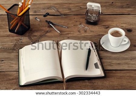 Open blank notebook on a wooden desk with a cup of black coffee, pencils, pens, paper clips, ruler and compass. Free space for text. Copy space. Closeup. top view
